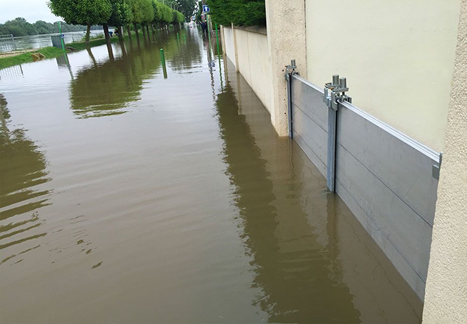 côté de maison fortement inondé avec une barrière anti inondation et des arbres au loin